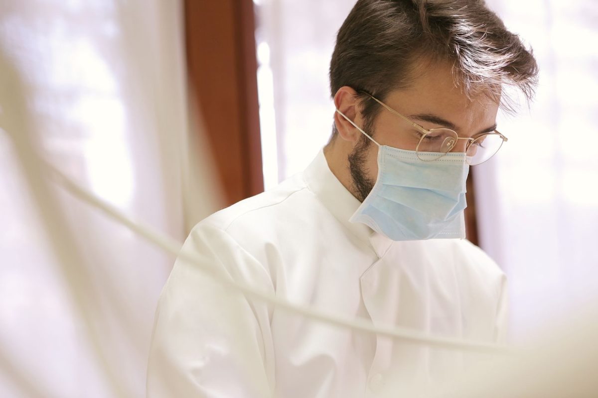 A male doctor focuses intently while wearing a face mask indoors.
