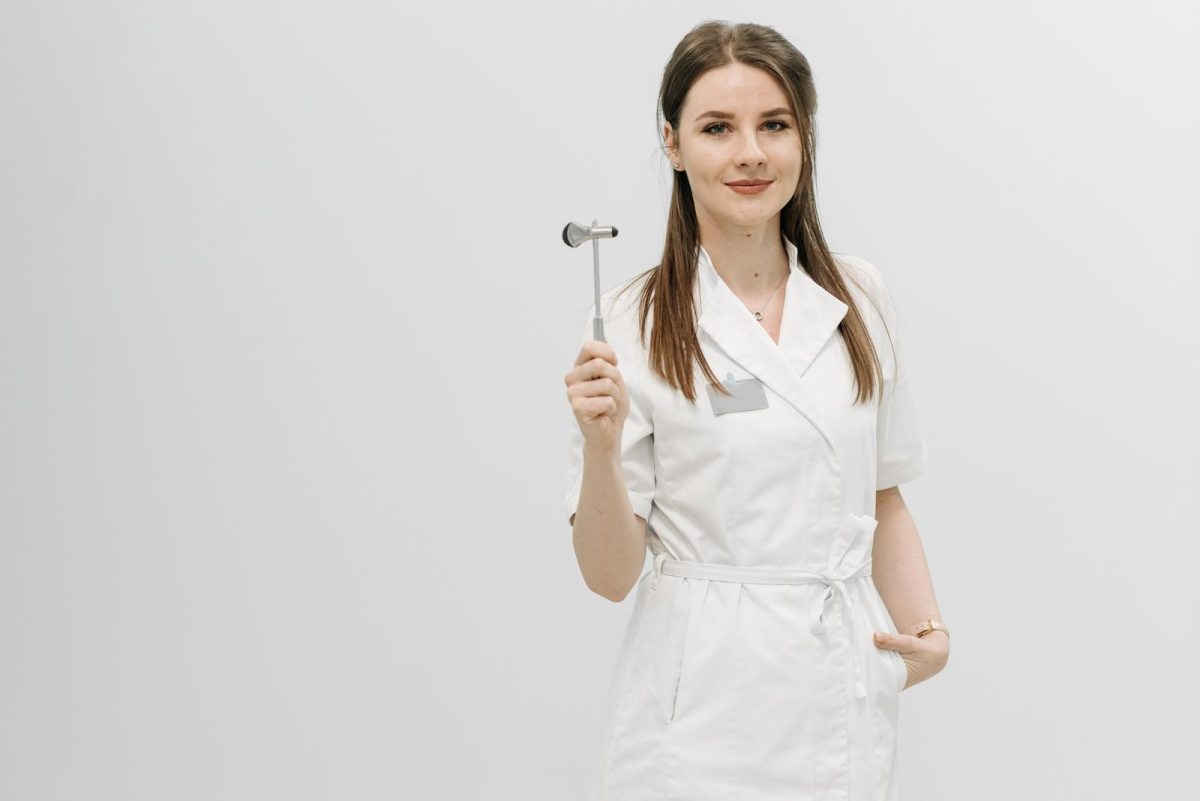 Female healthcare professional posing confidently in a white coat holding a reflex hammer.